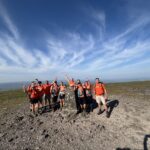 Group of Rotherham Hospice supporters in bright orange t-shirts celebrating at the summit during the Yorkshire Three Peaks Challenge to raise funds for local hospice care.