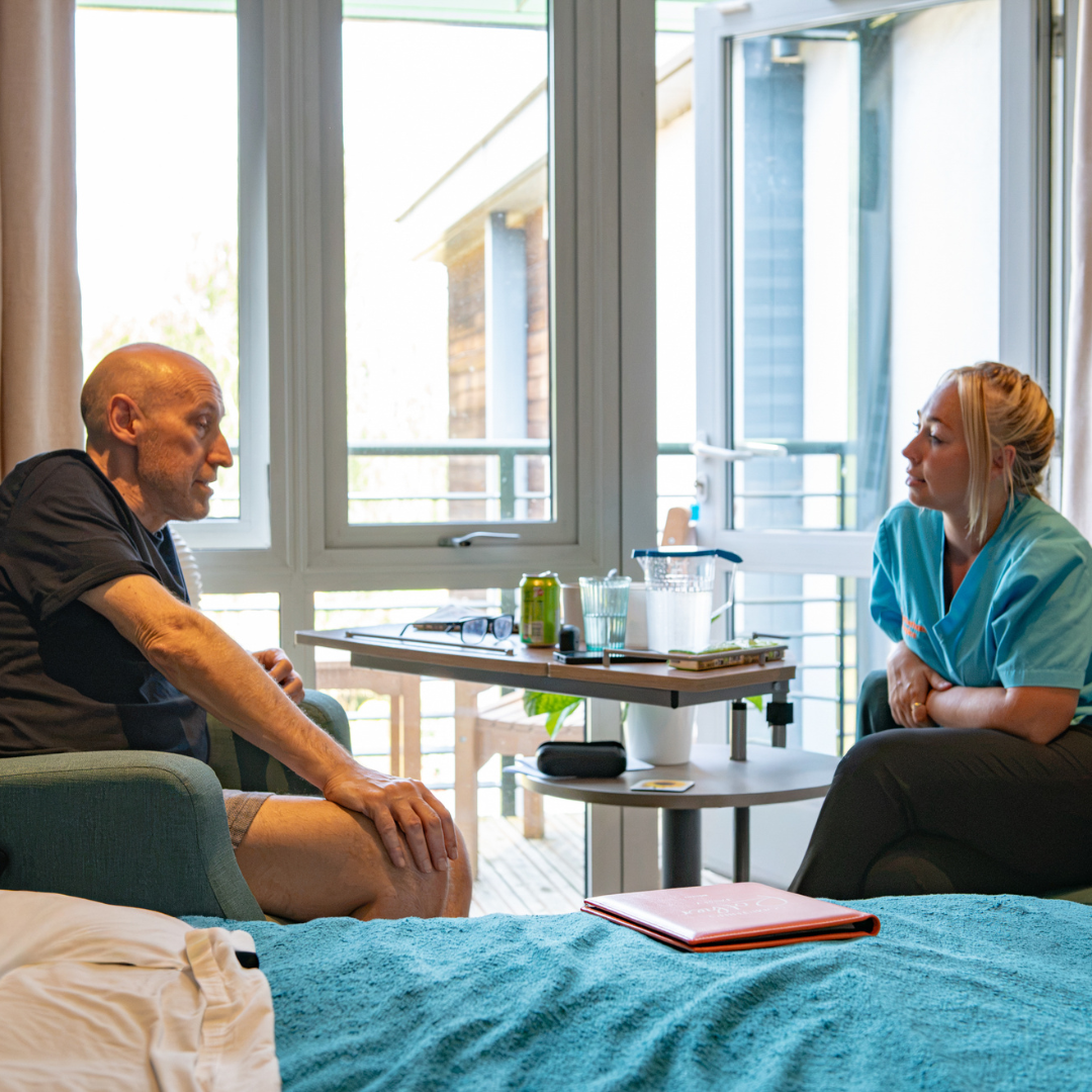 Rotherham Hospice nurse sitting and listening to a patient in a bright inpatient room with garden views