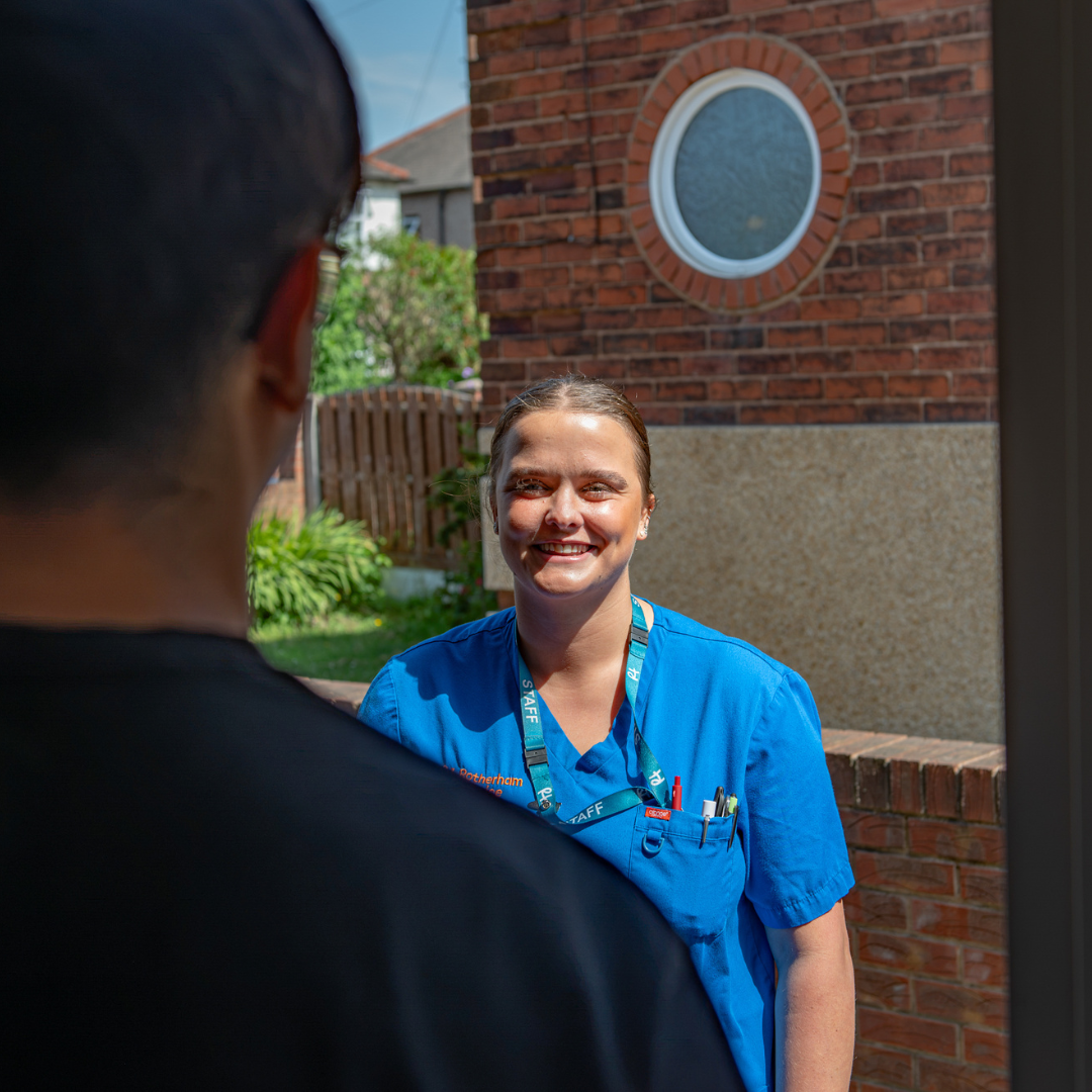 Smiling Rotherham Hospice community nurse greeting a patient at their front door during a home visit