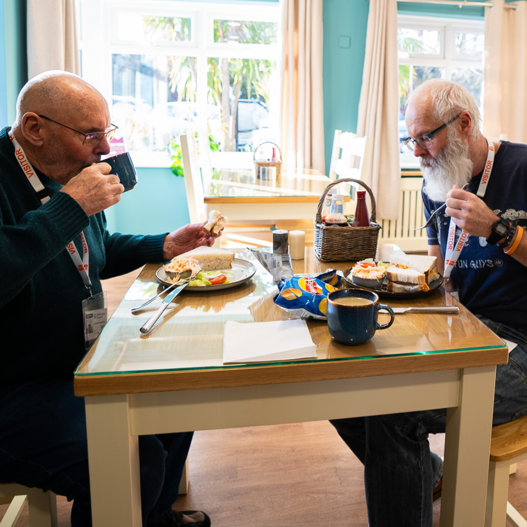 Two visitors enjoying sandwiches and hot drinks in the bright Rotherham Hospice café