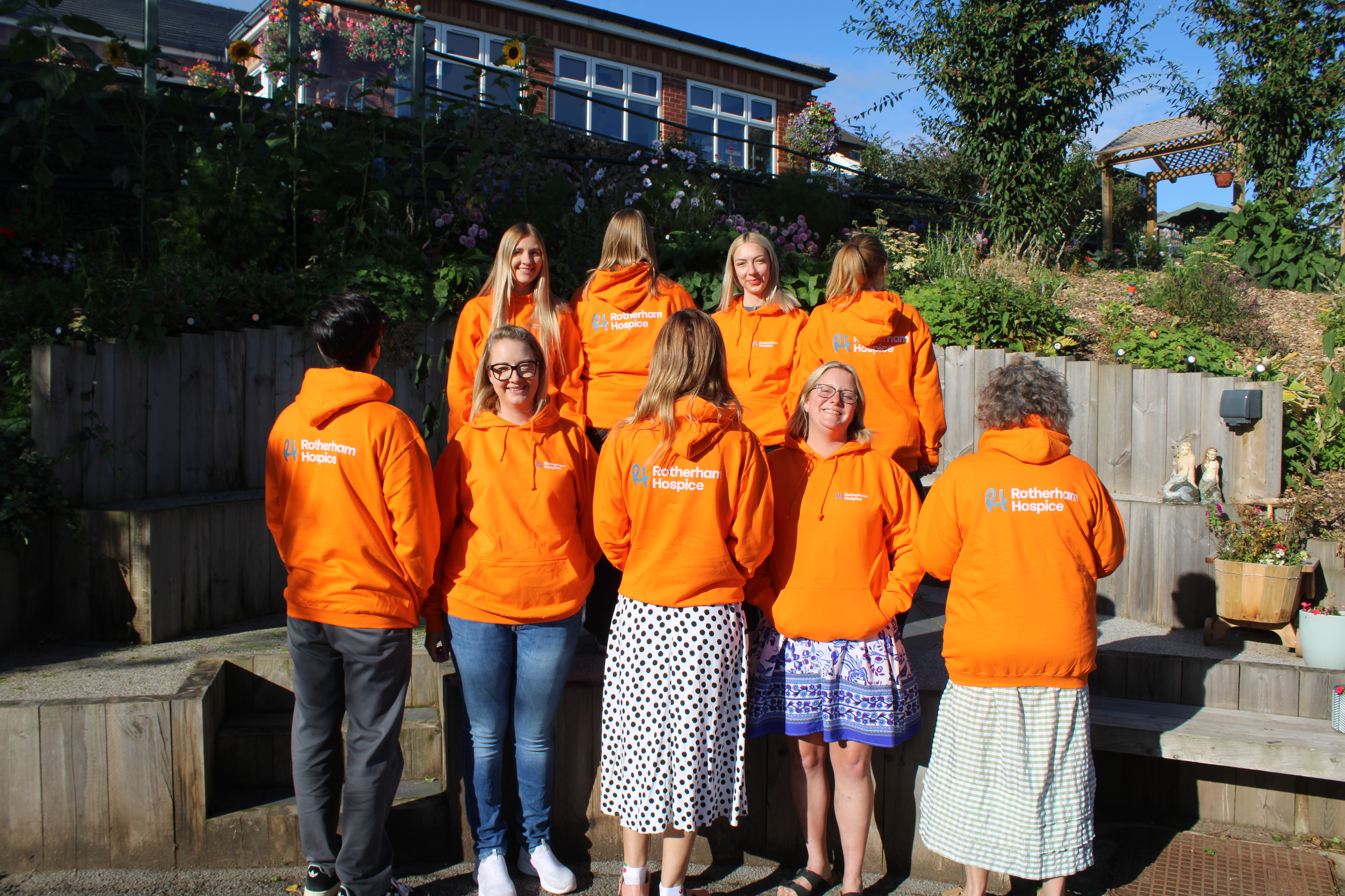 Rotherham Hospice team wearing free printed orange hoodies from Hoodie Hut's charity campaign, in the hospice garden